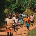 children running and walking on brown sand surrounded with trees during daytime